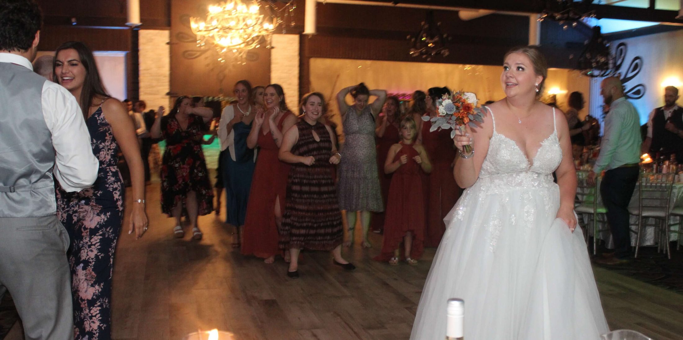 Bride looking back with flower bouquet, ready to toss the bouquet behind her to a crowd of girls gathered, as part of the "bouquet toss" tradition