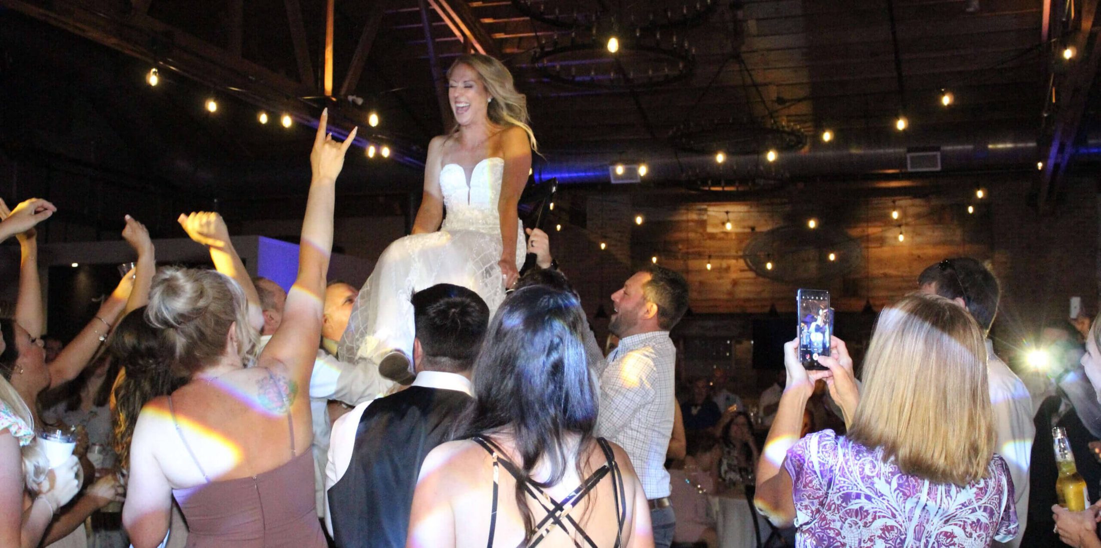 Bride held up on a chair in the middle of the dance floor, surrounded by people and hands in the air