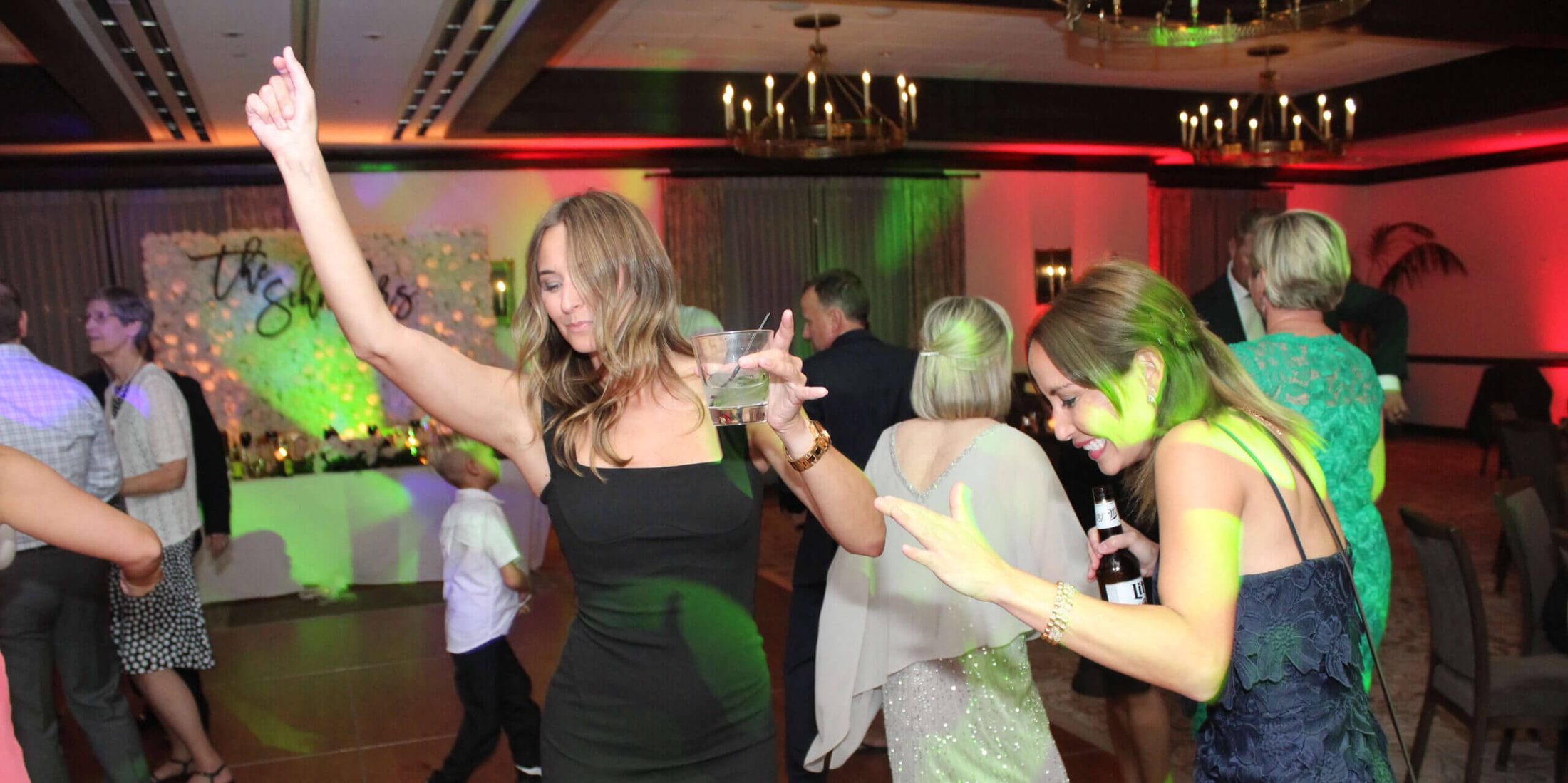 Two girls dancing with drinks in one hand and the other hand up in the air, on the dance floor of a wedding reception with the best Chicago area Wedding DJ, Paul Michaels Events