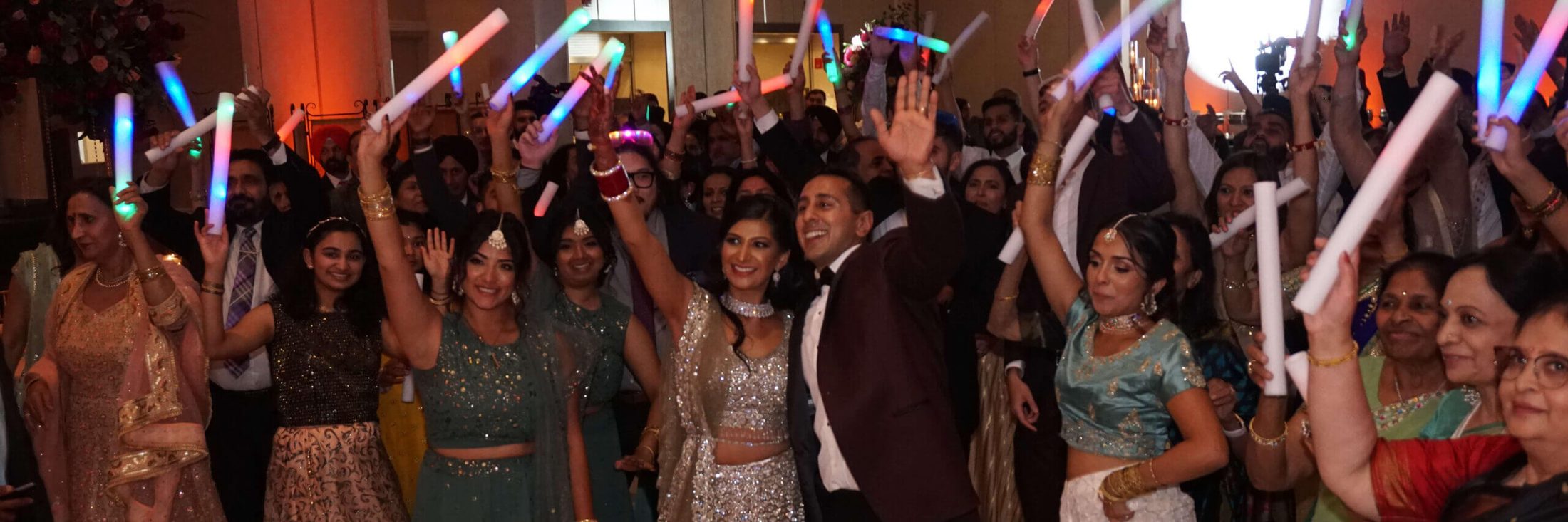 Bride and groom with friends and family behind them, with light sticks and hands in the air, having the best time with music and DJ services provided by Chicago area DJ company, Paul Michaels Events