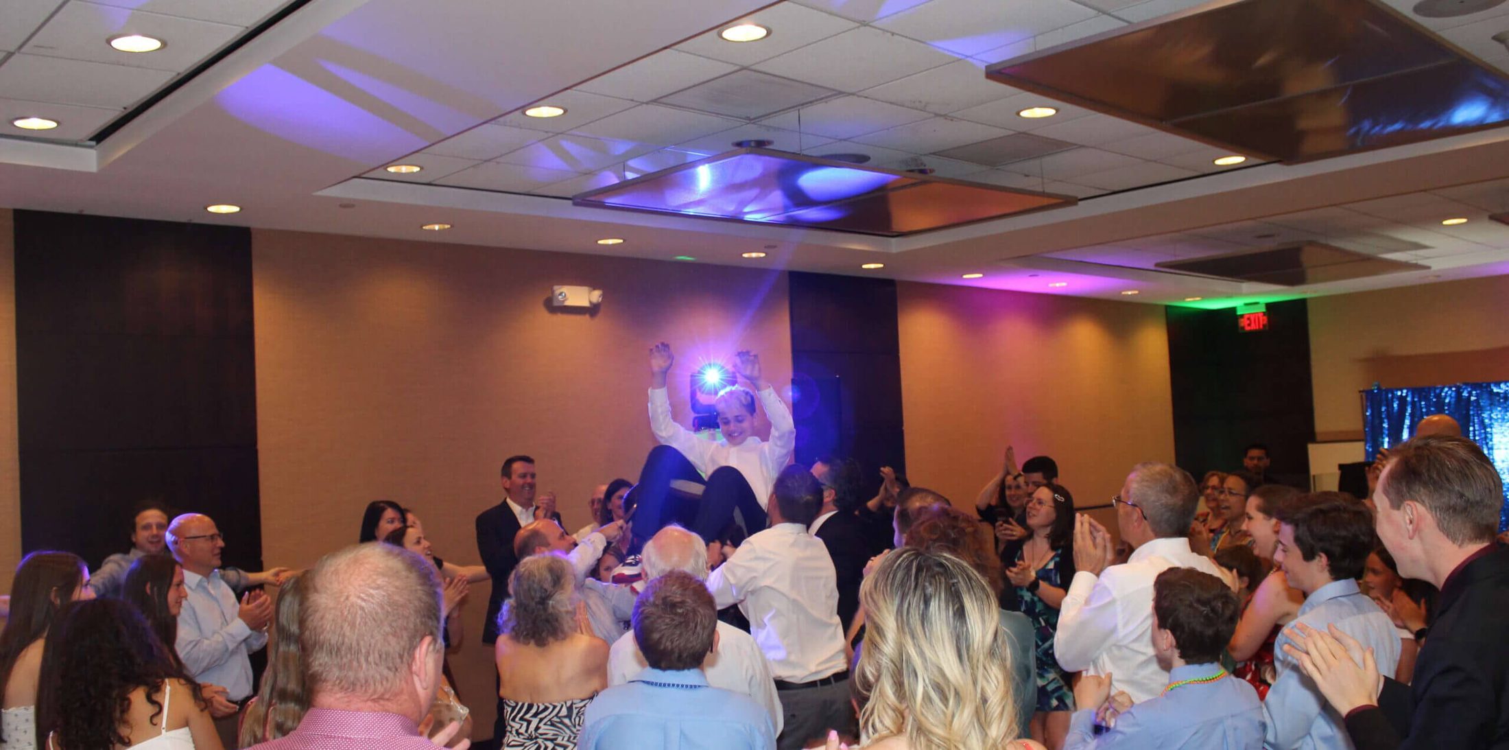Group of people surrounding guest of honor at bar mitzvah, with bar mitzvah entertainment services provided by Paul Michaels Events