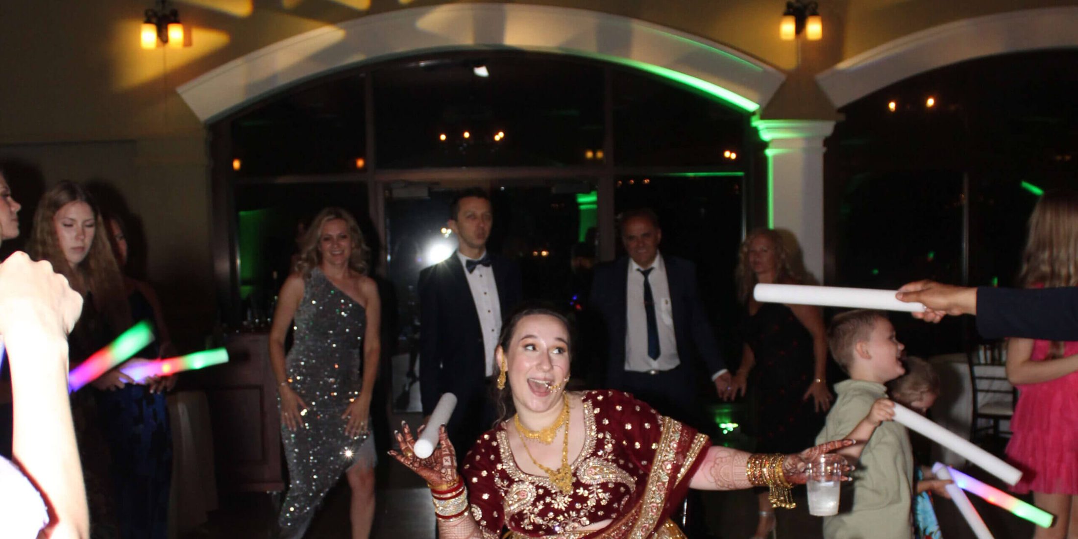 A bride in the middle of the dance floor surrounded by dancing guests and light up foam sticks, courtesy of Paul Michaels Events, a Premier Chicagoland DJ Company