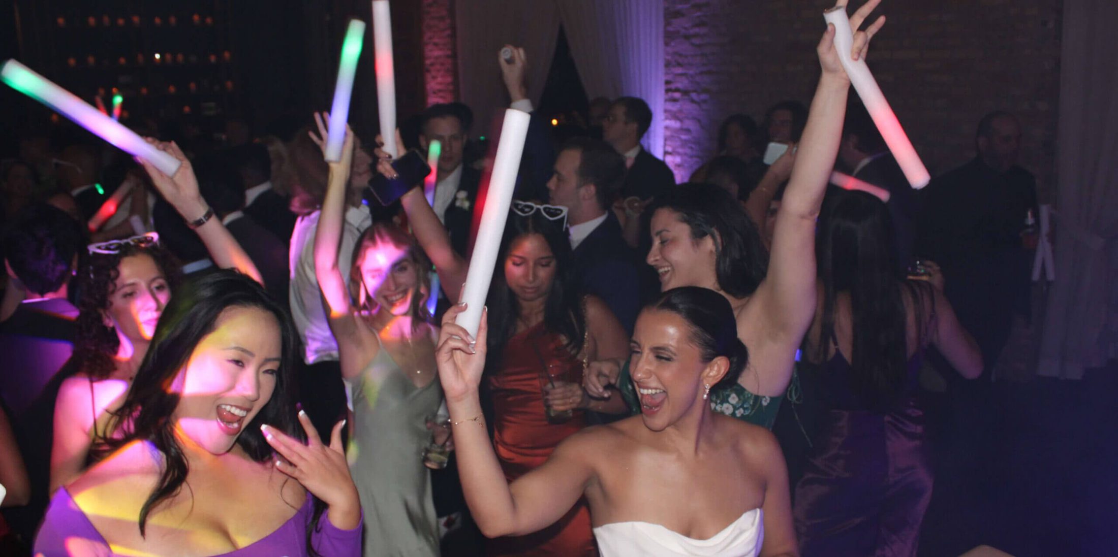 A dance floor filled with a bride and her guests, waving light up foam sticks and dancing along to the music played by Paul Michaels Events, the best bicultural wedding DJ services in Chicago