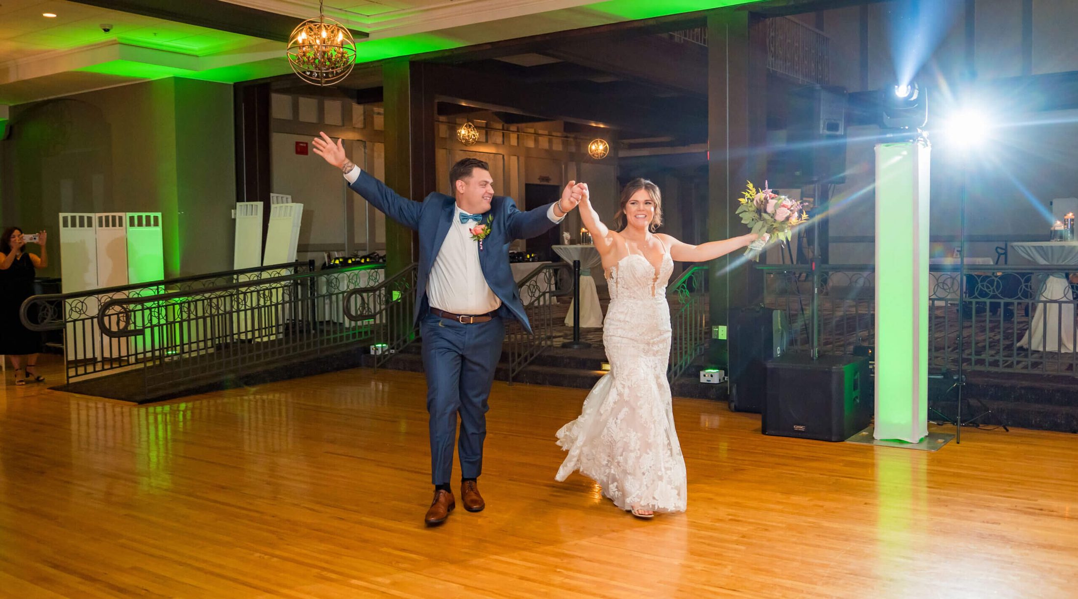 Bride and groom entering their reception with wide open arms.