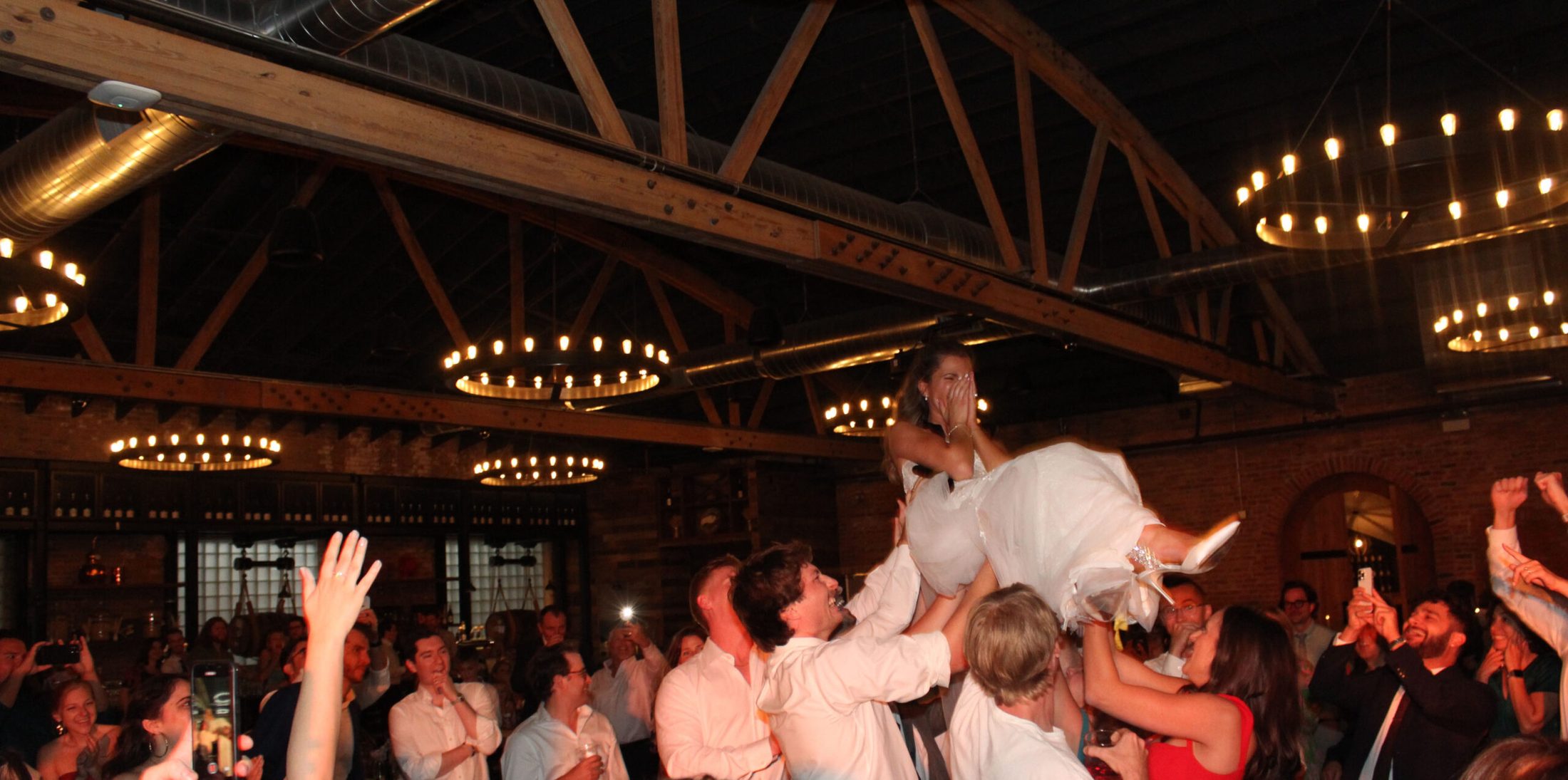 Bride getting lifted up by her crowd of guests at wedding event